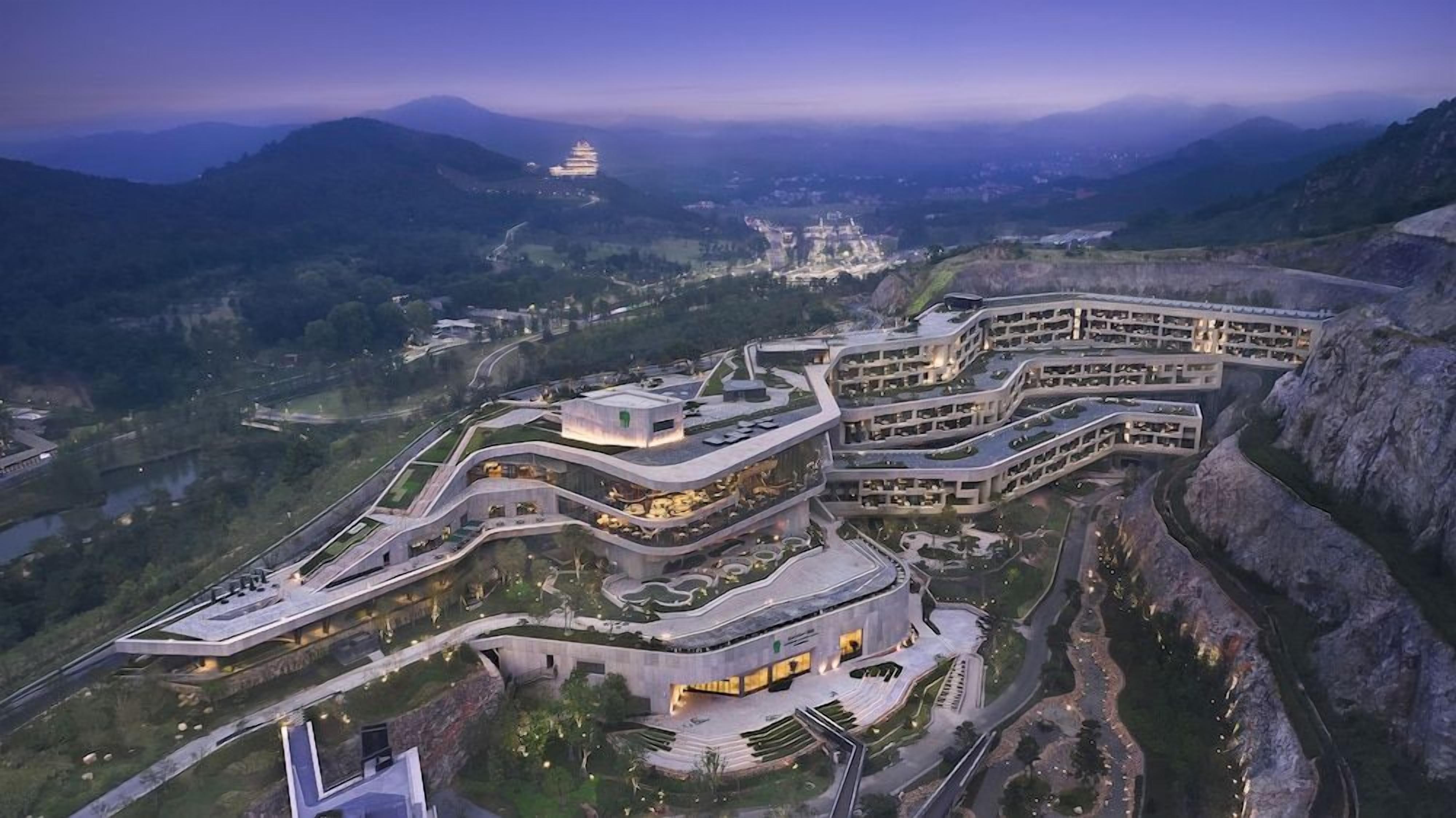 Un moderno complejo hotelero con varias edificaciones interconectadas, rodeado de un paisaje montañoso.