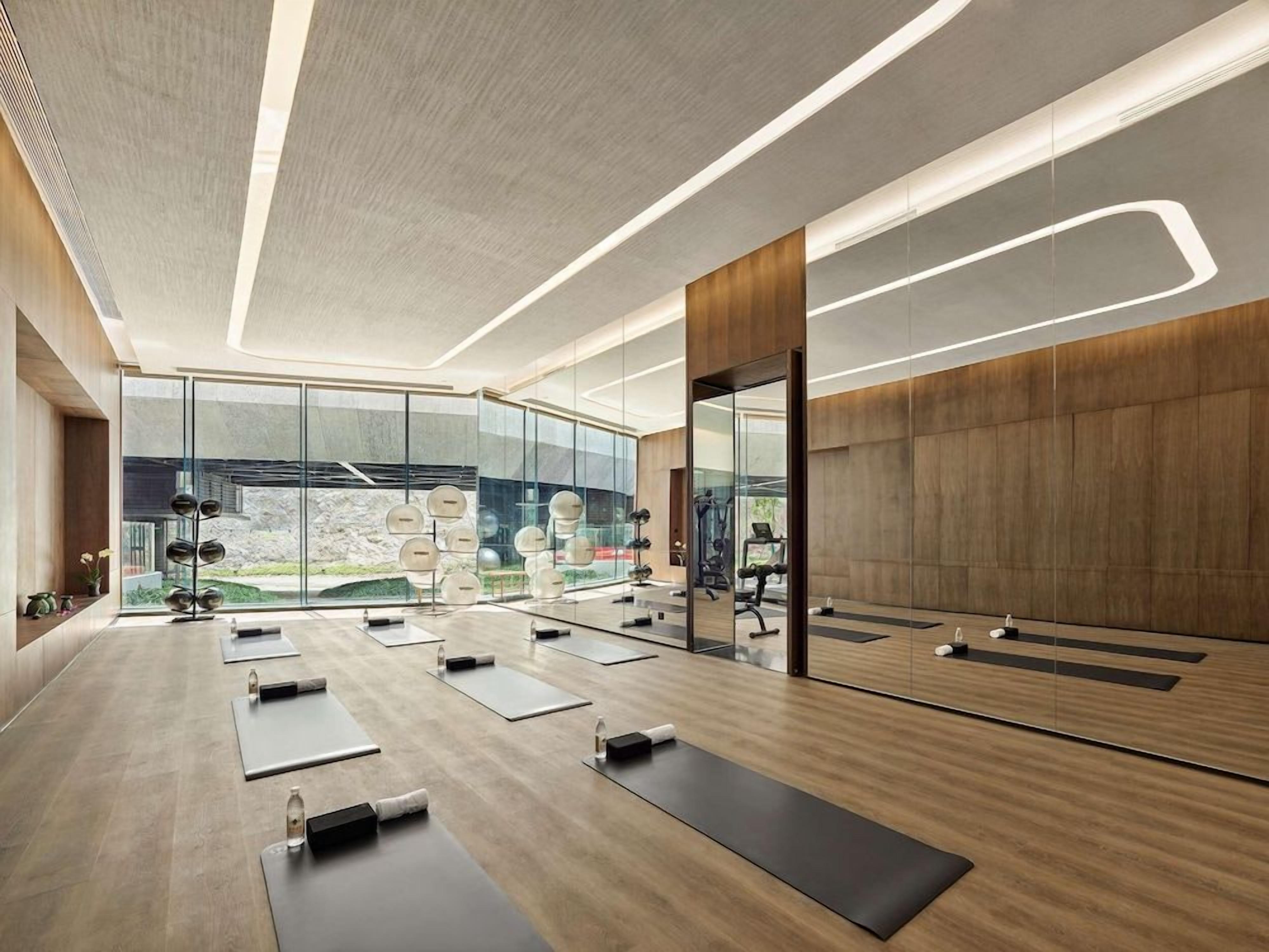 Un gimnasio moderno con colchonetas de ejercicio, un espejo grande y vistas al exterior.