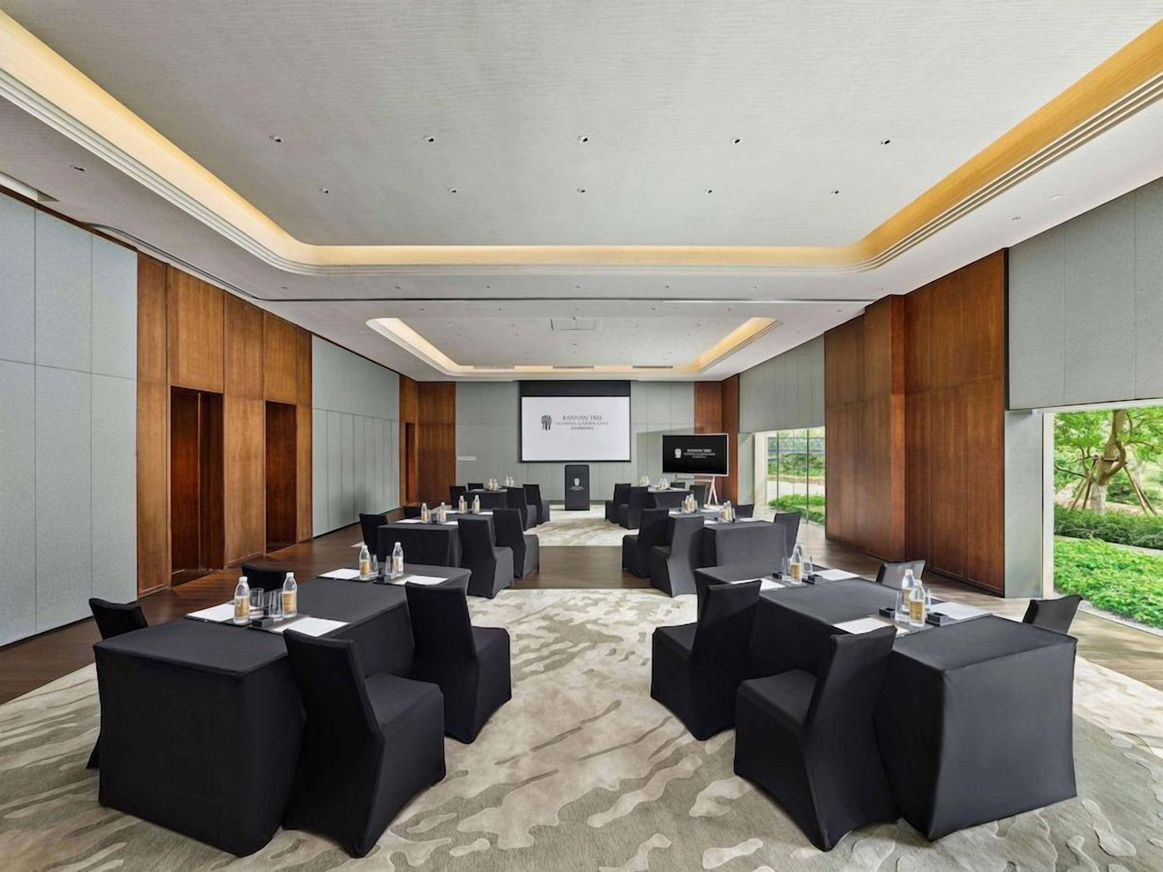 Un salón de conferencias con una pantalla grande, varias mesas y sillas dispuestas para una reunión.