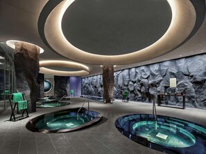 Un moderno espacio de spa con luces circulares en el techo, una gran pared de roca y varias tinas de hidromasaje.