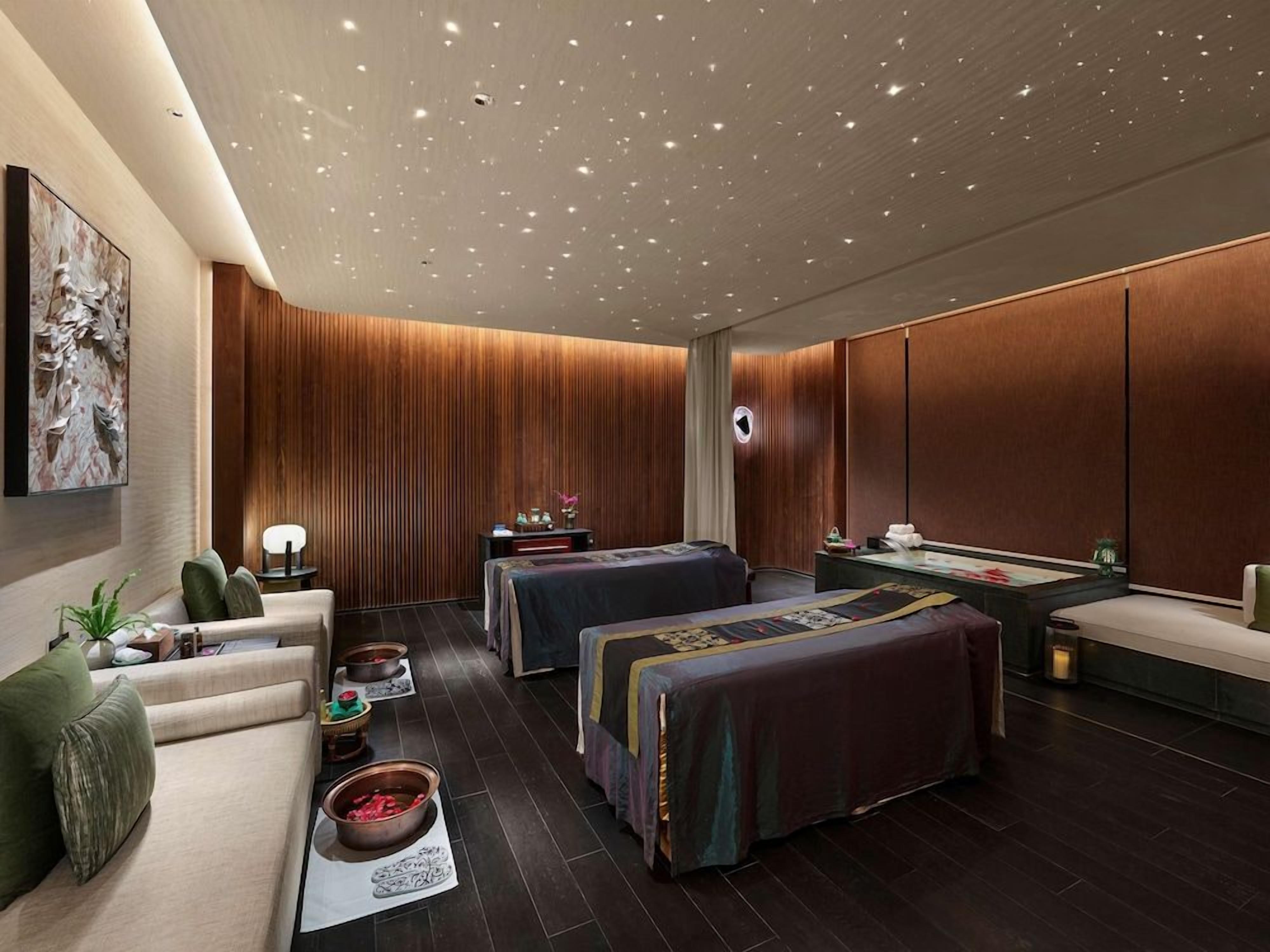 Un moderno spa con techo de madera, dos camillas de masaje, una mesa de masaje y un mostrador de recepción.