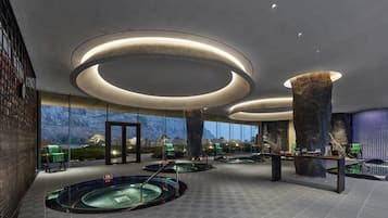A modern spa area with multiple hot tubs, a large rock centerpiece, and a view of mountains through large windows.