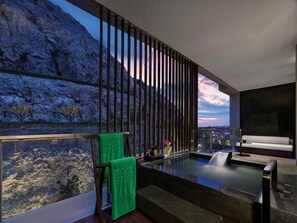 Un moderno cuarto de spa con un ventanal grande, un jacuzzi y vistas a un paisaje rocoso.