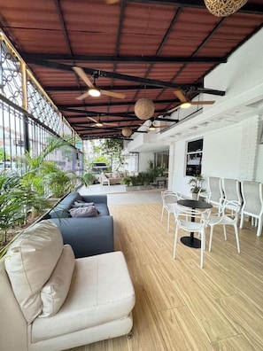 Un interior moderno con piso de madera, un sofá, una mesa de comedor con sillas y ventiladores de techo.