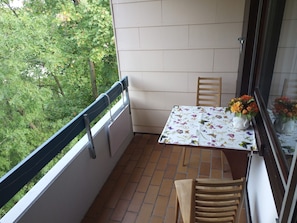 Un pequeño balcón con una mesa, sillas y un ventanal con vistas a zonas verdes.