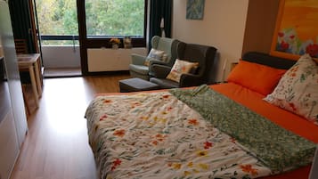 A bedroom with a bed, a sofa, a table, and a view of the outdoors.