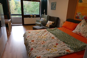 A bedroom with a bed, a sofa, a table, and a view of the outdoors.