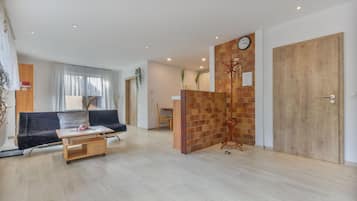 Ein modernes Wohnzimmer mit einer Couch, einem Couchtisch und einer Holzkommode. Eine Holztür und eine Uhr sind an der Wand zu sehen.