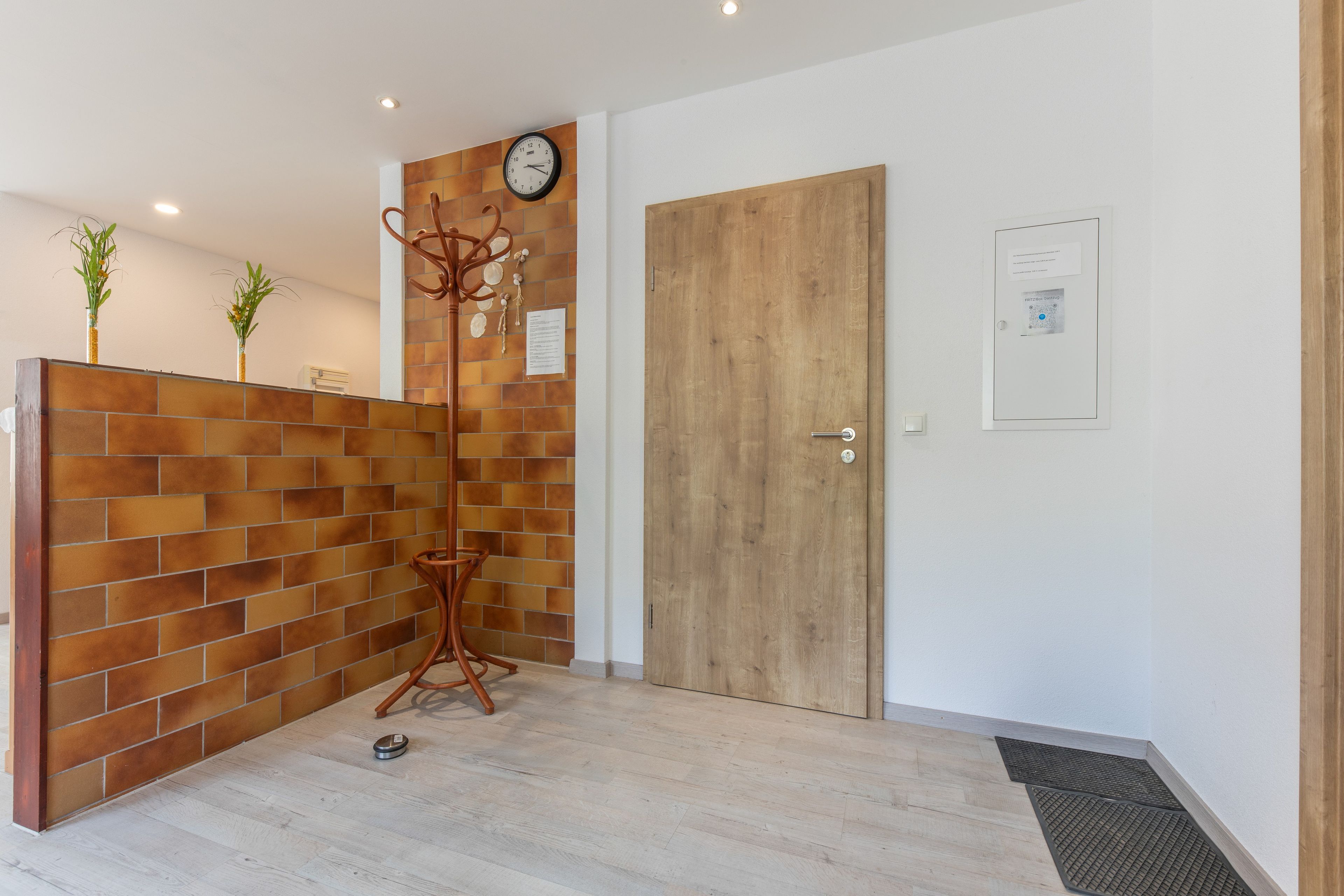 Uma área de recepção com um balcão de madeira, um relógio, uma porta e uma pequena planta na parede.
