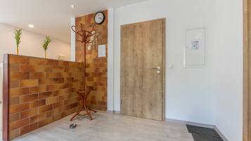 Zona de recepción con un mostrador de madera, un reloj, una puerta y una planta pequeña en la pared.