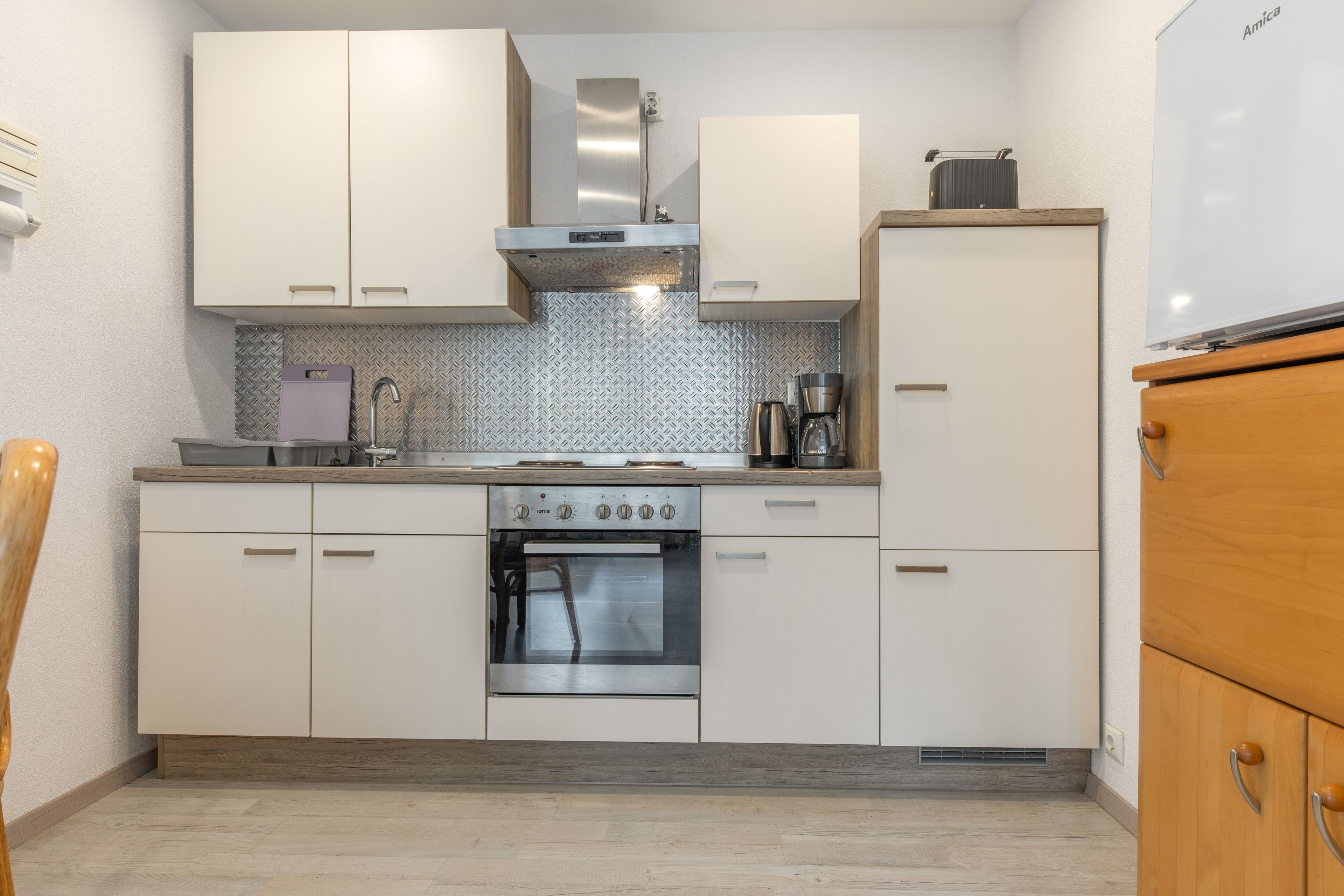 Una cocina compacta con armarios blancos, estufa de acero inoxidable y horno integrado.