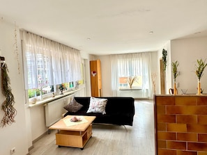 Un salon moderne avec un canapé, une table basse et un radiateur. On y trouve des fenêtres avec des rideaux, une porte et un mur en briques.
