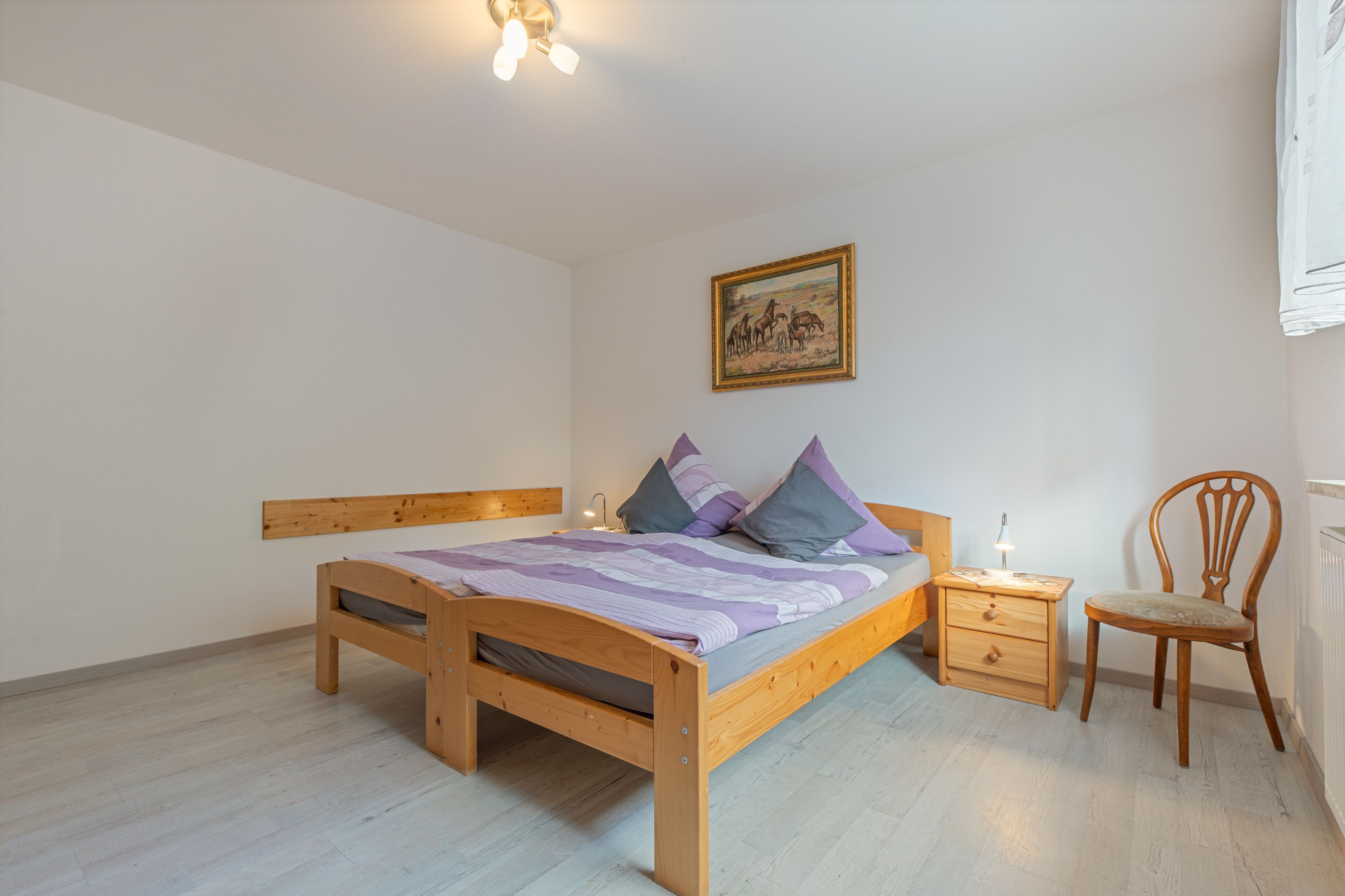 Ein Schlafzimmer mit einem hölzernen Bett, einem Nachttisch, einem Sessel und einem Bild an der Wand.