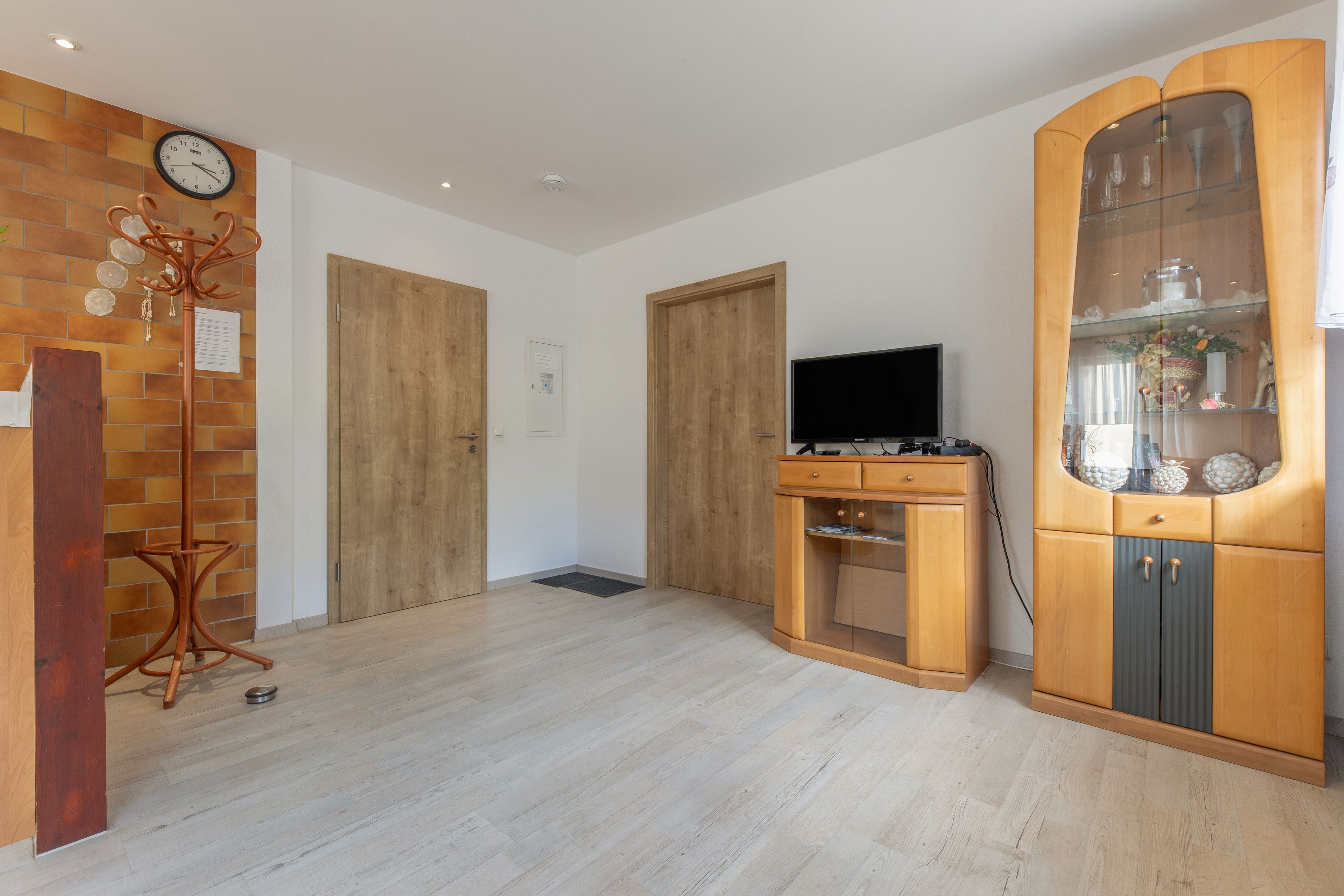 A room with a wooden floor, a television on a wooden stand, and a cabinet with glass doors.