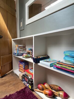 A room with a wooden wardrobe, a mirror, and shelves containing board games, coloring books, and wooden spoons. - The Crow and Stone - Great Location (Fly Creek)