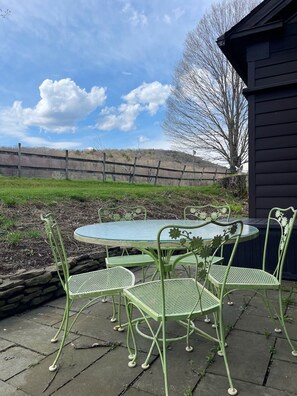 A patio with a round table and four chairs, surrounded by a stone wall and a wooden fence. - The Crow and Stone - Great Location (Fly Creek)