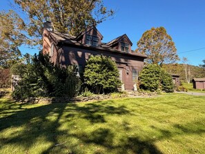 A two-story house with a stone foundation, surrounded by a well-maintained lawn and various trees. - The Crow and Stone - Great Location (Fly Creek)