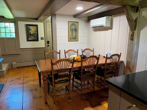 A dining area with a wooden table and chairs, a painting on the wall, and an air conditioning unit. - The Crow and Stone - Great Location (Fly Creek)