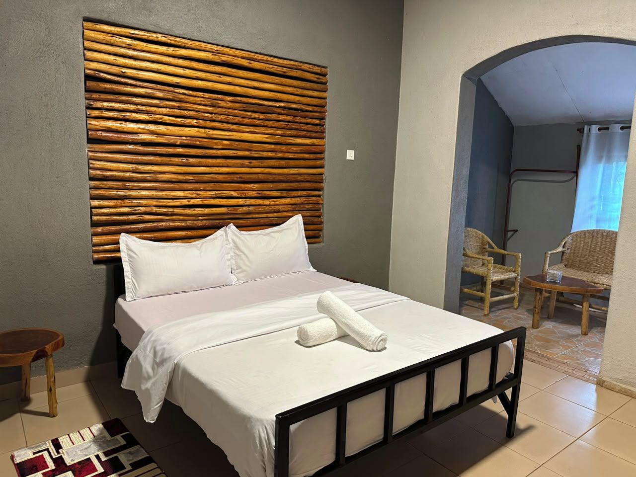 Una cama con ropa blanca, un cabecero de madera y una toalla enrollada sobre la cama.