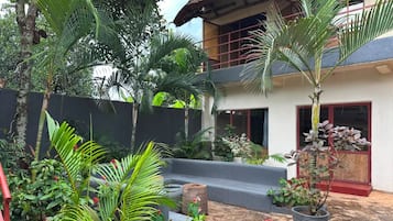 Un patio con plantas en macetas, suelo de piedra y un edificio con puerta roja.