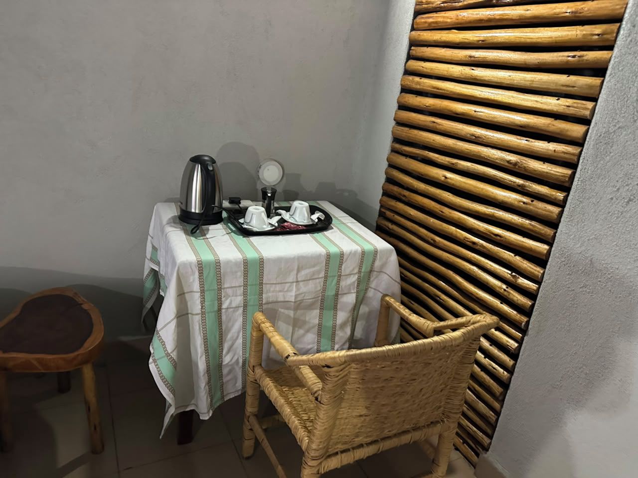 Una habitación pequeña con una mesa preparada para dos, una silla de mimbre y una pared con diseño tejido.
