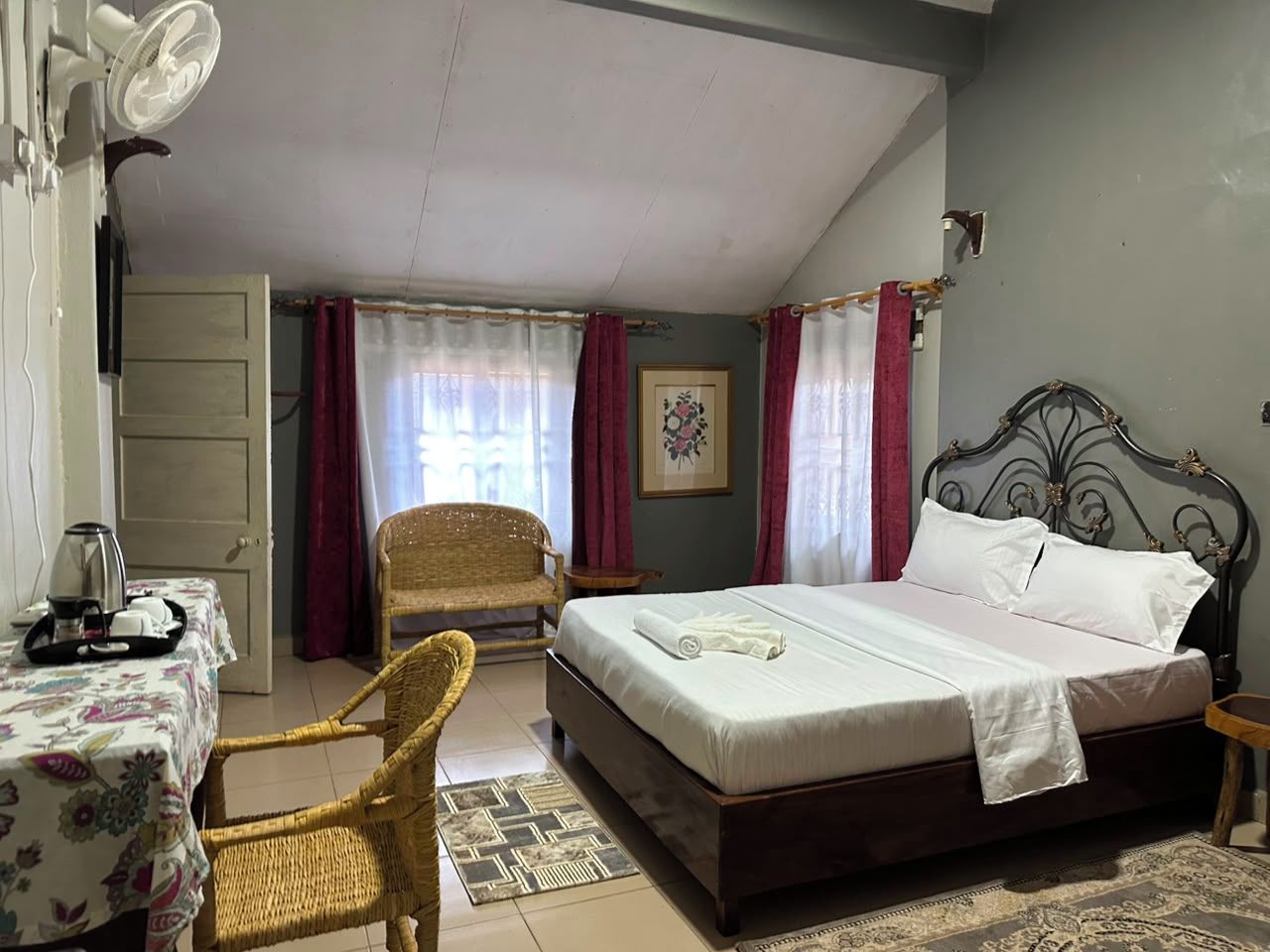 Quarto com cama, cadeira, mesa e chaleira, e um ventilador.