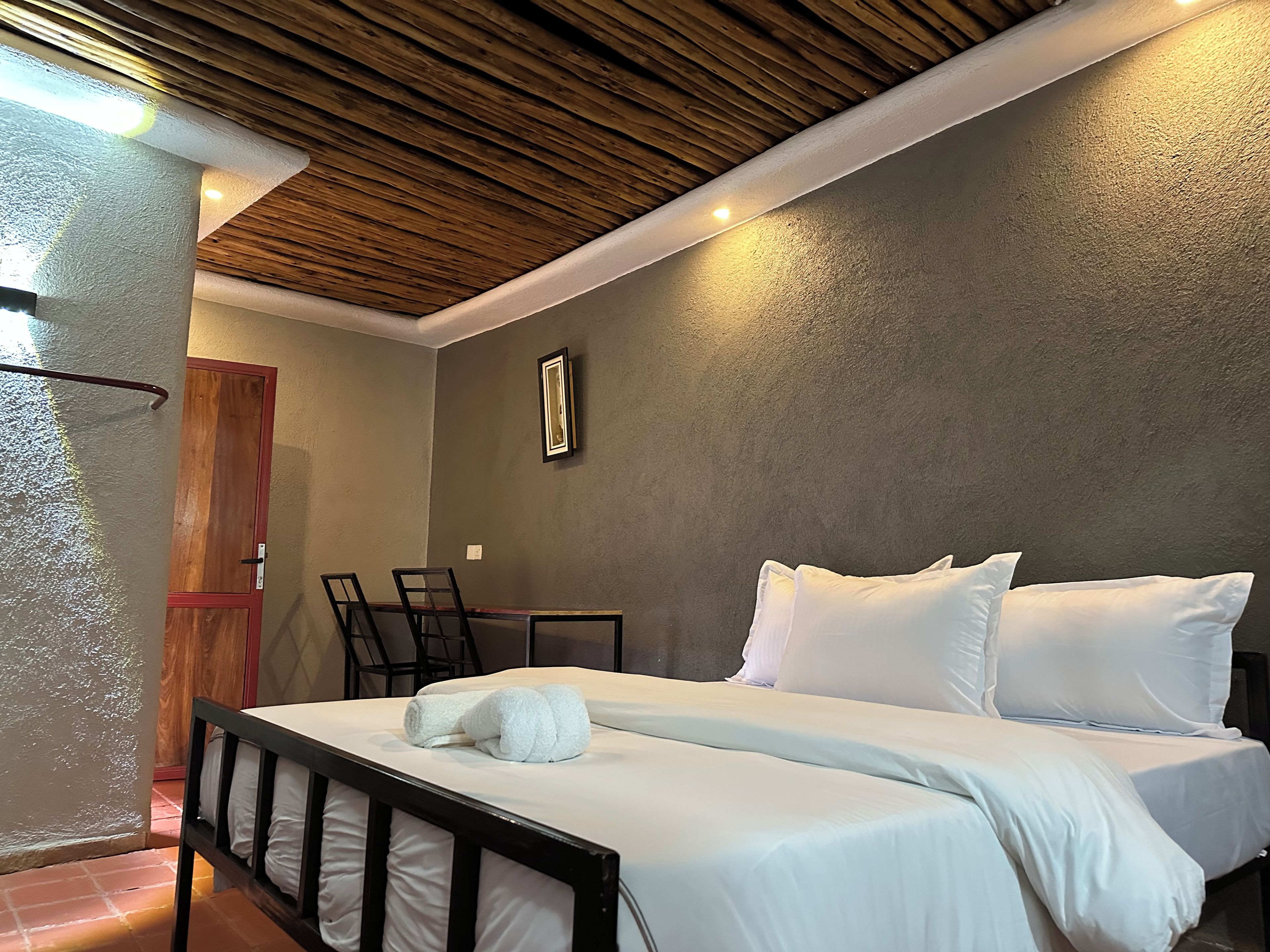 A hotel room with a bed, bedside tables, a wooden ceiling, and a door.