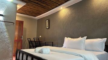 A hotel room with a bed, bedside tables, a wooden ceiling, and a door.