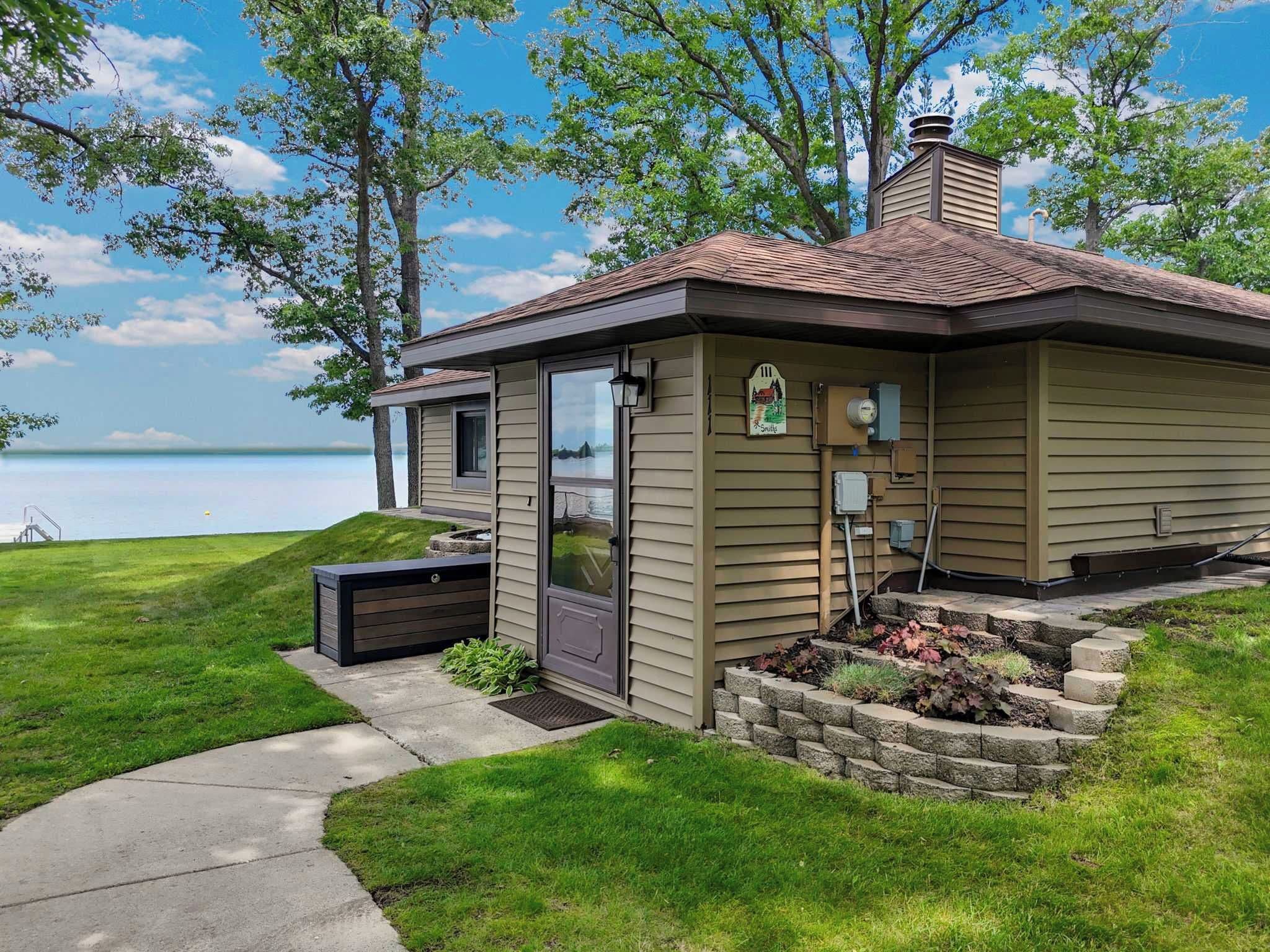 Une petite maison avec vue sur un lac, une cheminée et un jardinière en pierre.