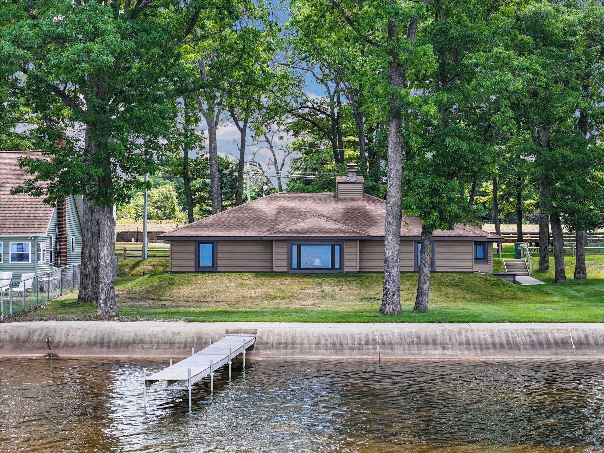 A house with a dock extending into a body of water, surrounded by trees and a grassy area.