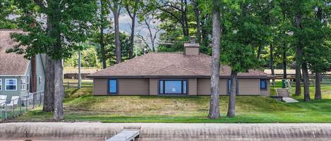 A house with a dock extending into a body of water, surrounded by trees and a grassy area.