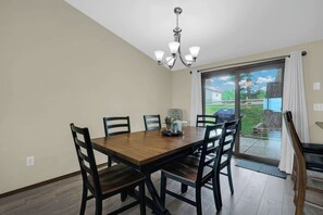 A dining area with a wooden table and chairs, a chandelier, and a view through a glass door to the outdoors. - Lakeside Cottage - Dock, Views, Fireplace (Prudenville)