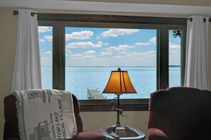 A room with a view of a lake, a lamp on a table, and two chairs. - Lakeside Cottage - Dock, Views, Fireplace (Prudenville)