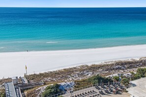 A beach with a clear view of the ocean, a sandy shore, and a building with outdoor seating. - Luxurious Direct Gulf Front Penthouse (Miramar Beach)