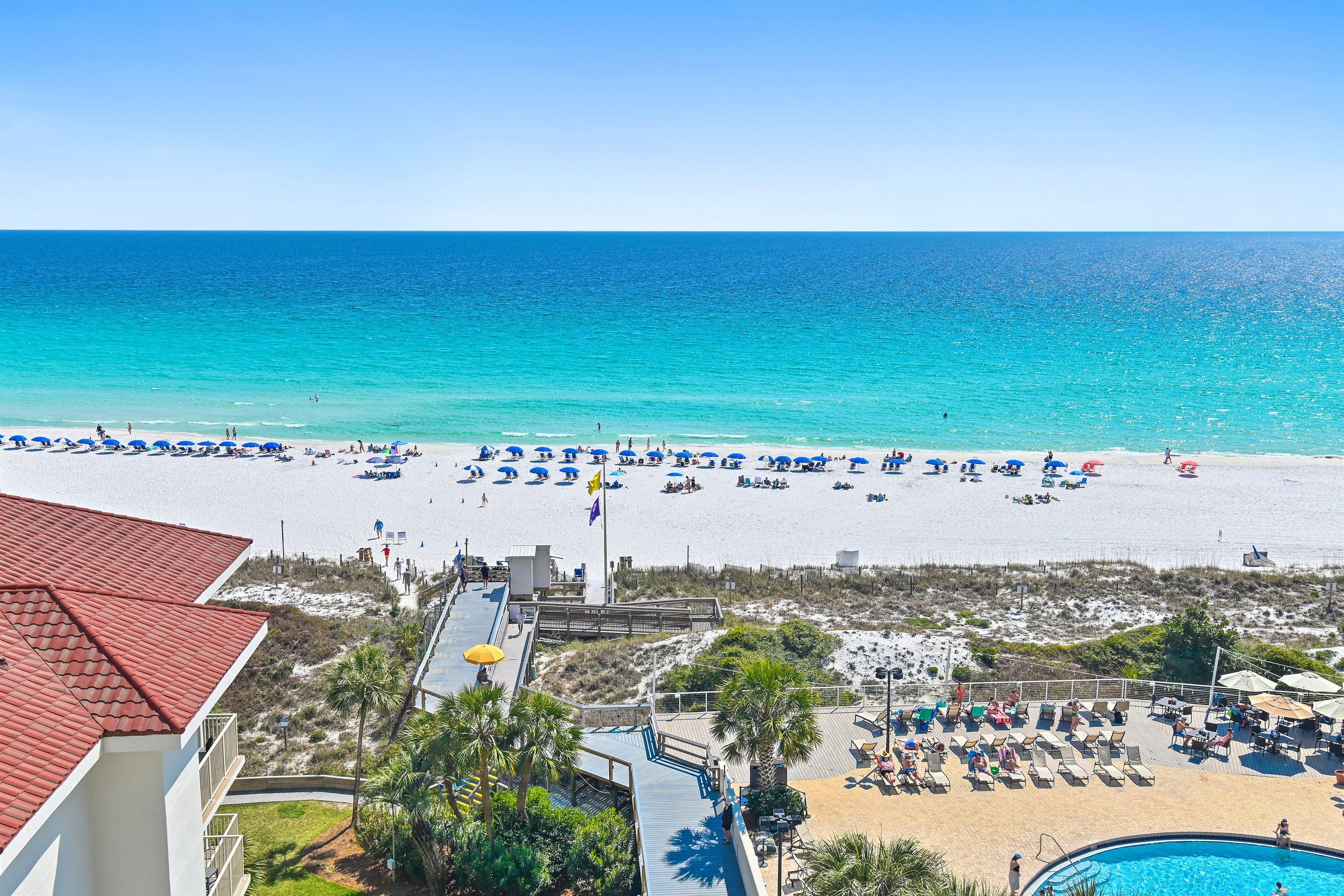 A beach resort with a pool, beach umbrellas, and a view of the ocean.