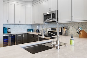 A modern kitchen with white cabinets, a stainless steel sink, and a built-in microwave. - Luxurious Direct Gulf Front Penthouse (Miramar Beach)