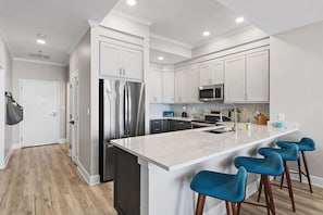 A modern kitchen with white cabinetry, stainless steel appliances, and a central island with bar stools. - Luxurious Direct Gulf Front Penthouse (Miramar Beach)
