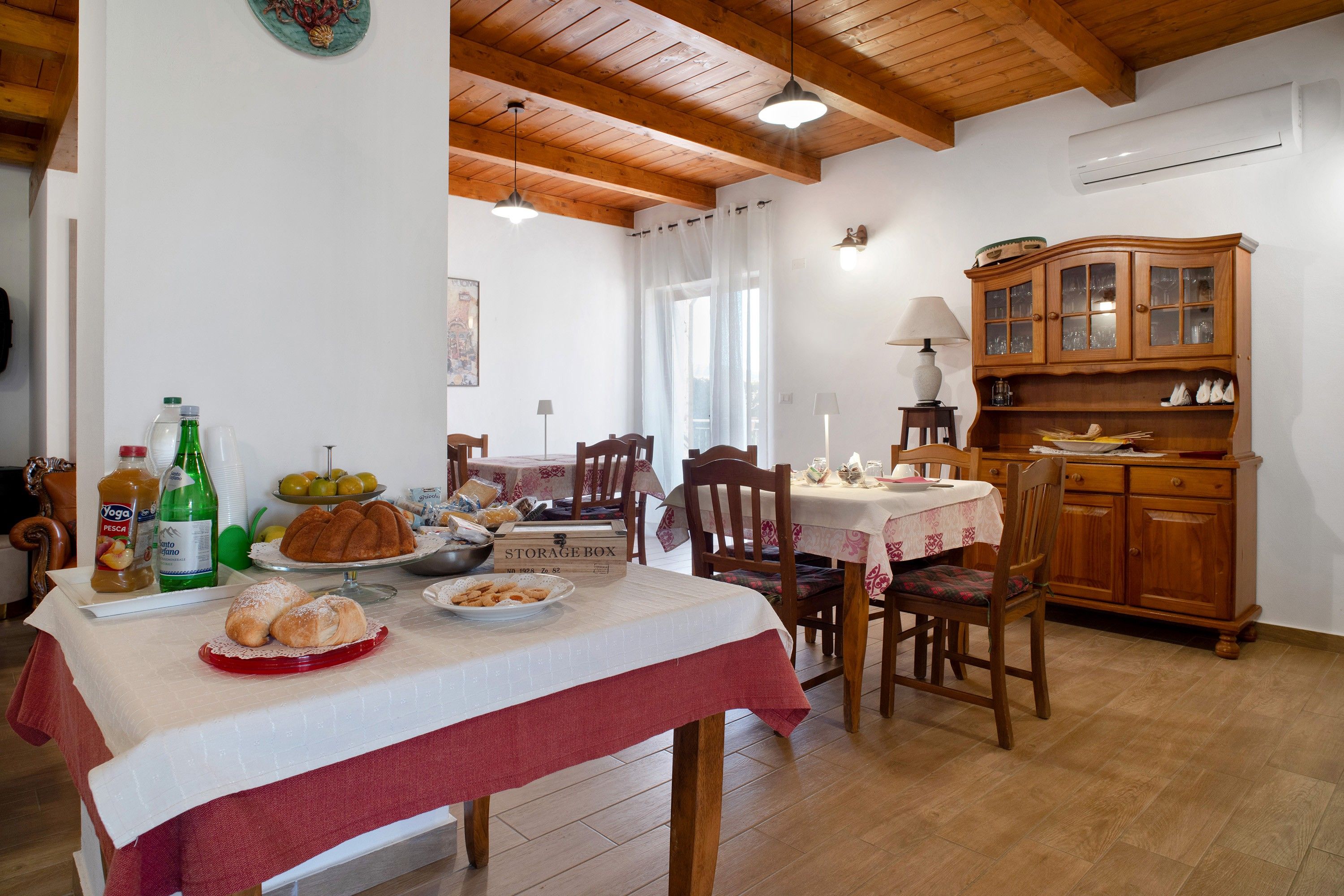 Uma sala de jantar com uma mesa posta para dois, um armário de madeira e um ar condicionado fixado na parede.