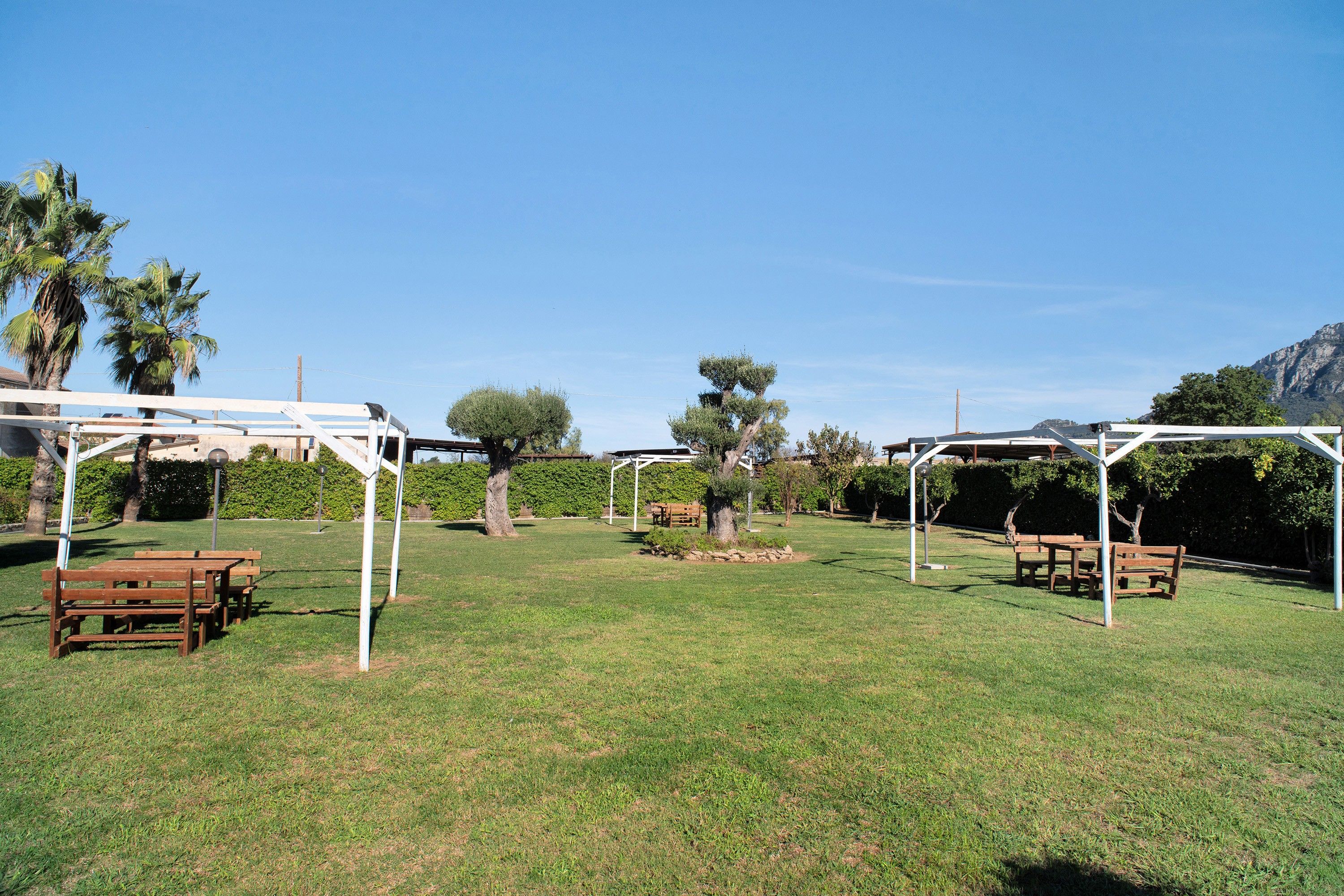 A grassy outdoor area with picnic tables and a pergola structure.