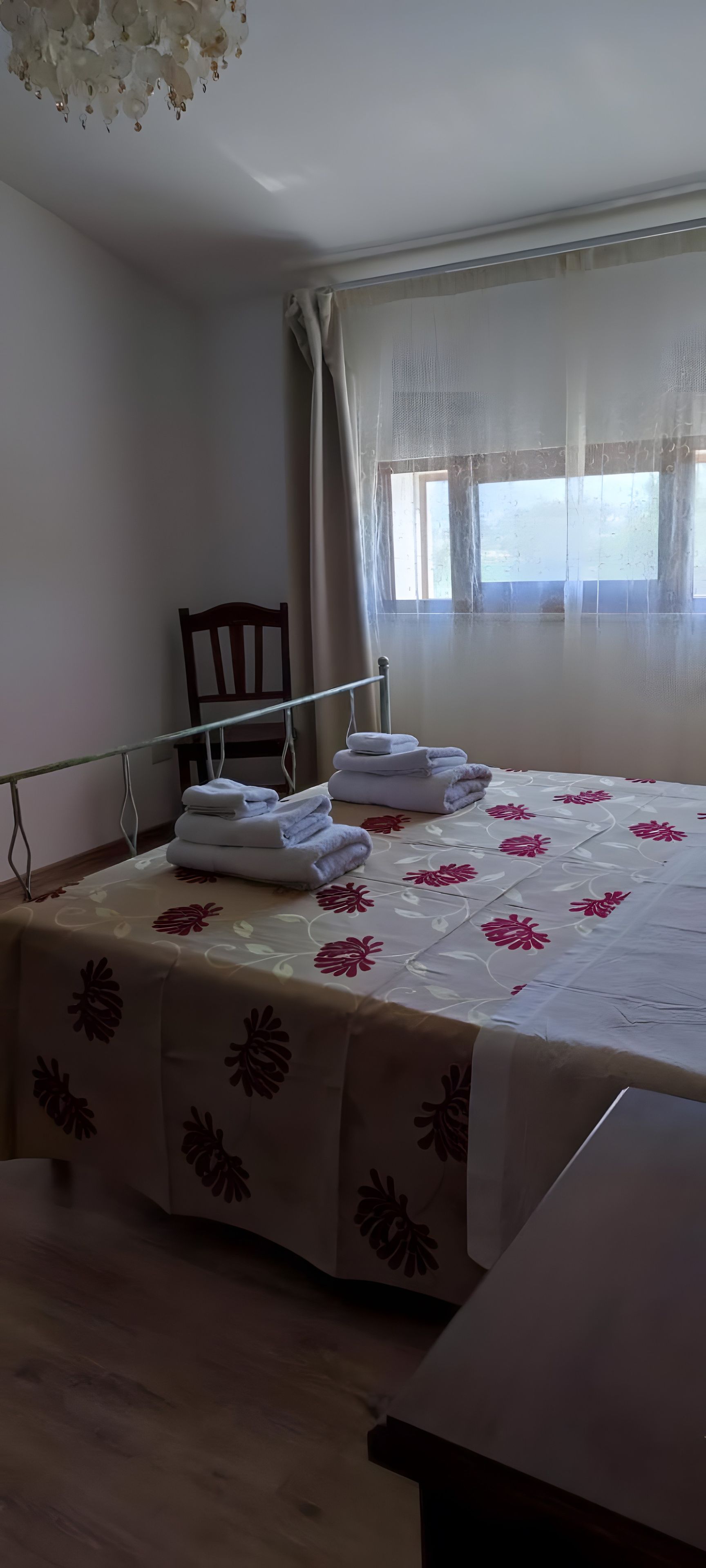 A bedroom with a bed, a chair, a window with curtains, and a ceiling light fixture.