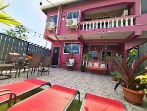 A pink building with outdoor seating, including chairs and a swing, and potted plants. - Canaan Beauty (Golden Grove)