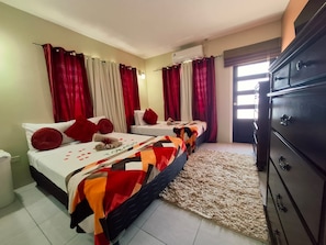 Habitación de hotel con dos camas, cortinas rojas y blancas, un armario grande y suelo de baldosas.