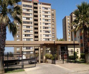 Un edifici residencial de diversos pisos amb entrada tancada, palmeres i un cel serè.