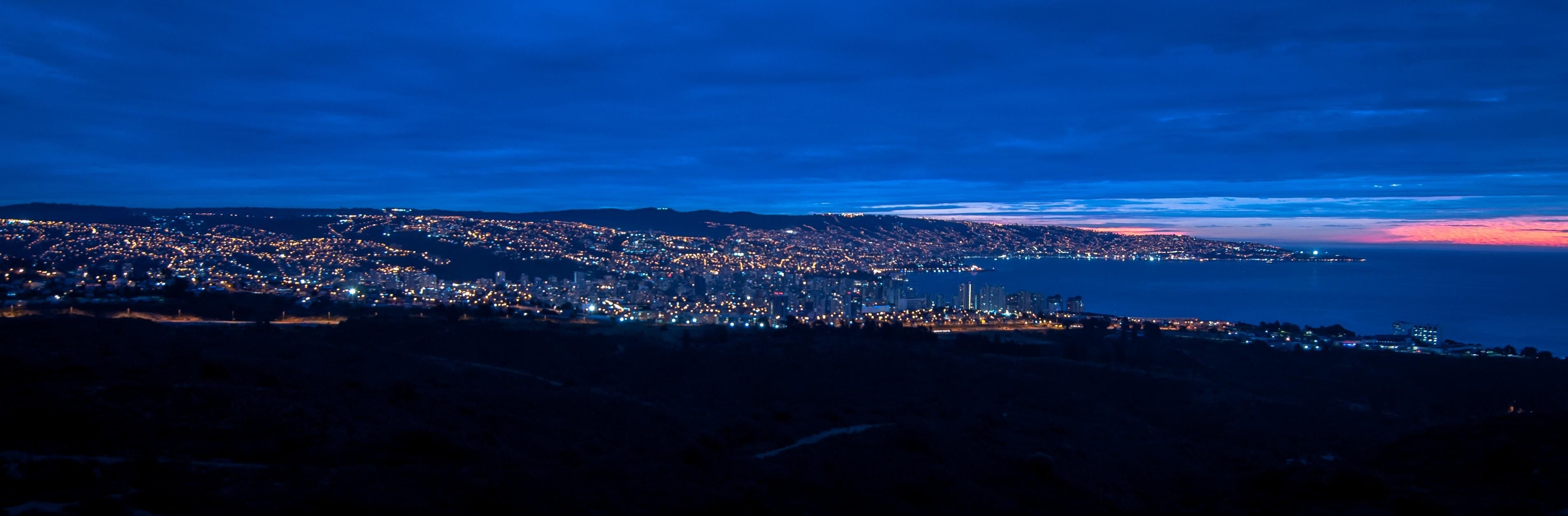 A coastal cityscape at dusk with a view of the ocean and a distant sunset.