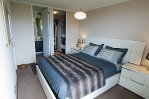 A bedroom with a bed, bedside tables, a nightstand, a lamp, and a hanging light fixture. - Viña Lounge (Vina del Mar)