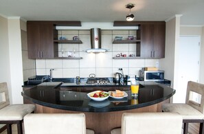 A kitchen with a central island, dark wooden cabinets, a stainless steel range hood, and a microwave. - Viña Lounge (Vina del Mar)