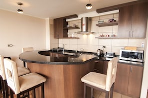 A modern kitchen with a central island, bar stools, a microwave, and a toaster. - Viña Lounge (Vina del Mar)