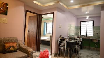 A living room with a sofa, a dining table with chairs, a kitchen area with a sink, and a bedroom with a bed.