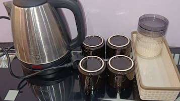 Une bouilloire en acier inoxydable, quatre tasses et un récipient en verre, le tout posé sur une surface réfléchissante.