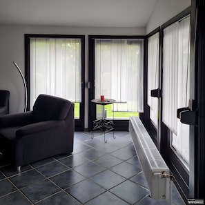 A modern living room with a dark sofa, a small round table with a red cup, and a radiator. - Holiday Home 'Haus "Marschenring"' with Private Terrace, Private Garden and Wi-Fi (Butjadingen)